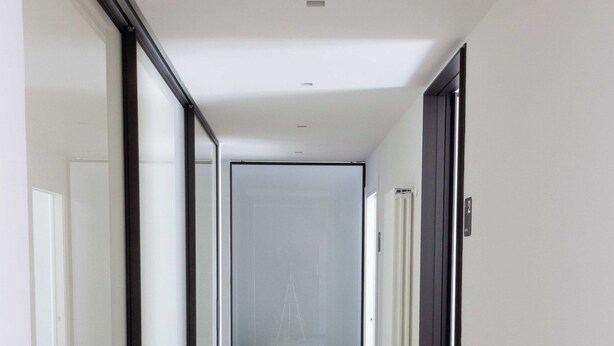 A modern hallway with a wooden floor, glass doors, and a frosted glass wall at the end.