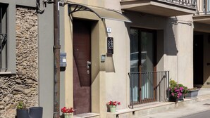 A building with a stone facade, a brown door, and a balcony with potted plants.