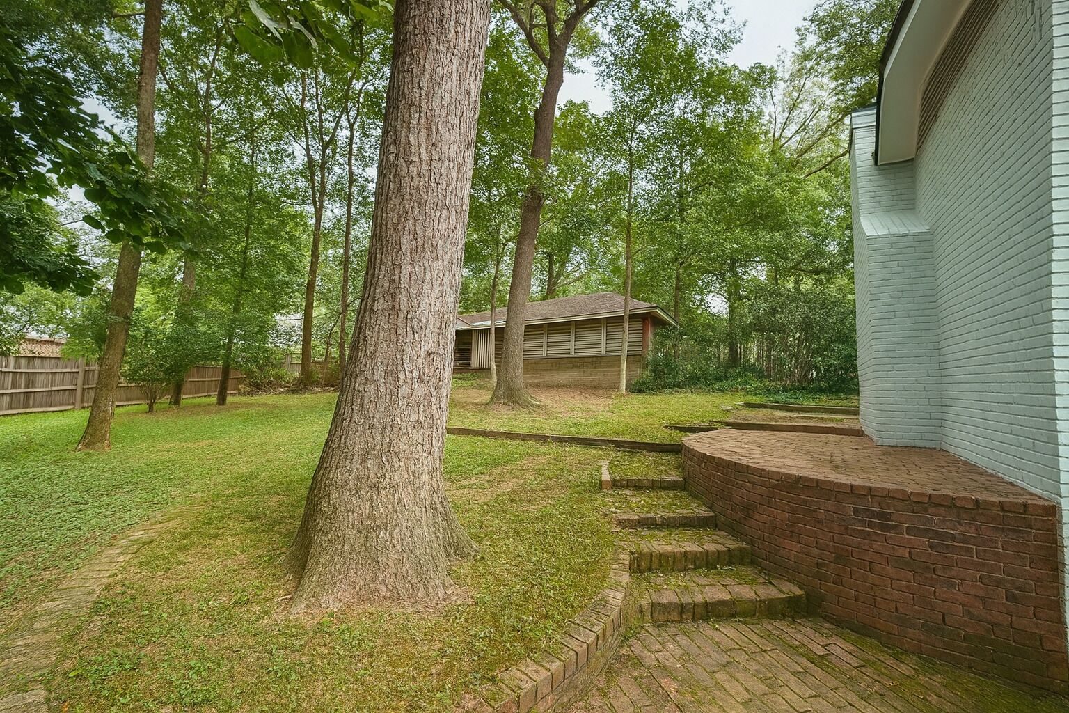 Un patio trasero con un muro de contención de ladrillo, una terraza de madera y una casa con techo inclinado.