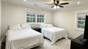 Un dormitorio con dos camas, ventilador de techo y ventanas con persianas.