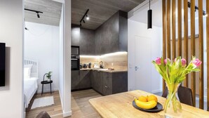 A modern kitchen with dark cabinetry, a wooden countertop, and a built-in oven. There is a dining area with a wooden table and a vase of flowers.