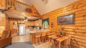 Interno di una baita in legno con cucina, zona pranzo e una scala che conduce a un piano superiore.