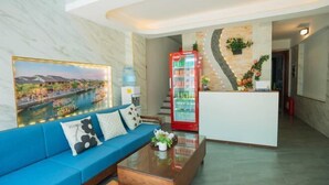 Un hall de hotel con un sofá azul, una recepción, un refrigerador y un dispensador de agua en la pared.