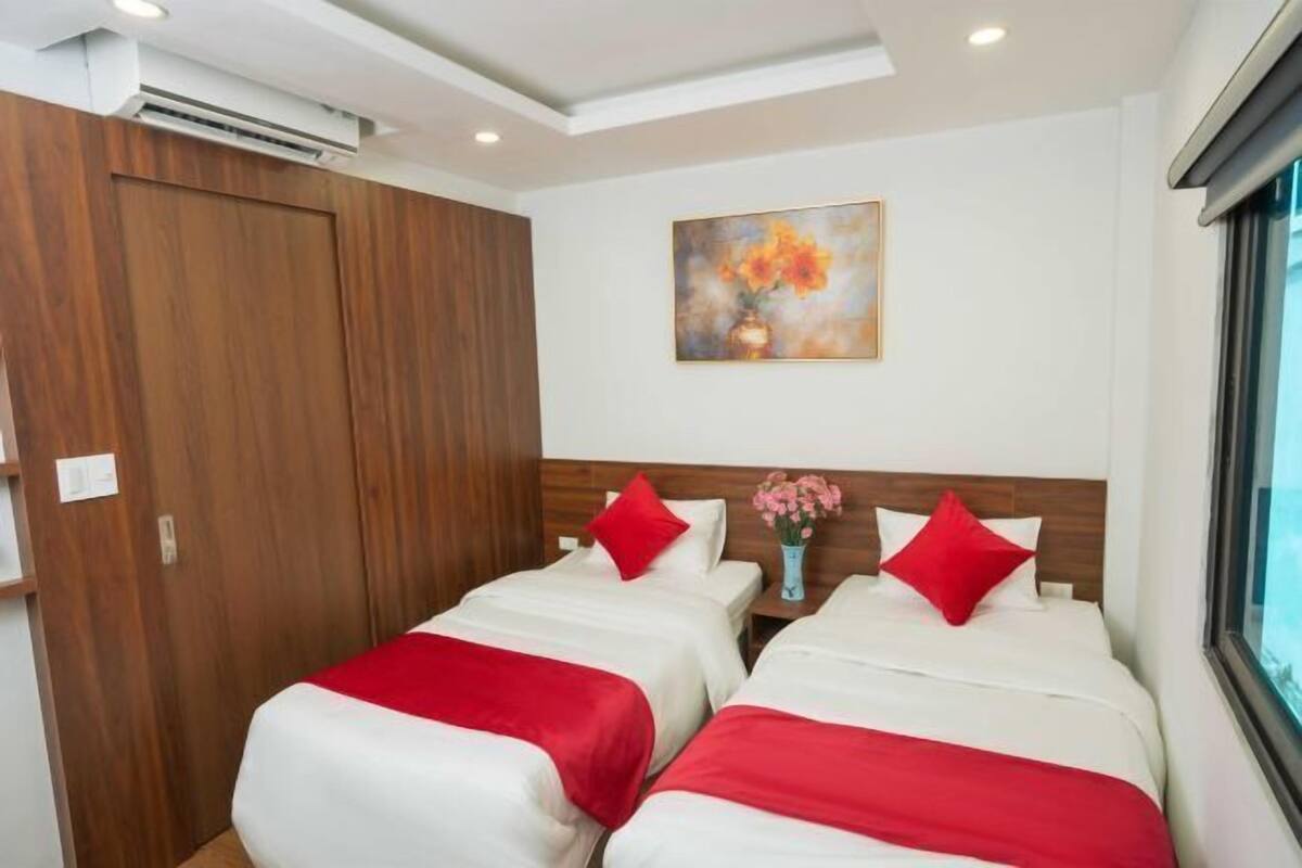 A hotel room with two beds, a wooden wardrobe, a painting on the wall, and a window.