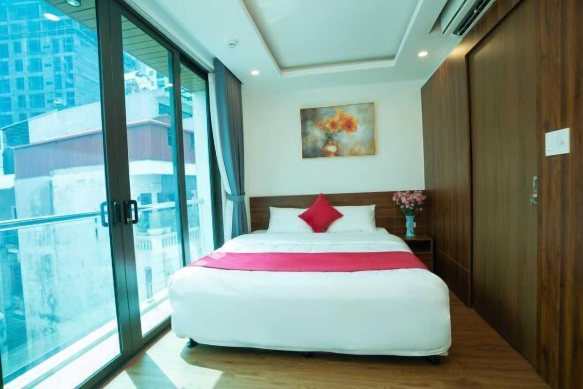 A hotel room with a large bed, a painting on the wall, and a view of the city through the window.