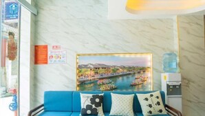 Un sofá azul con cojines estampados, un dispensador de agua y un cuadro con una vista de río.