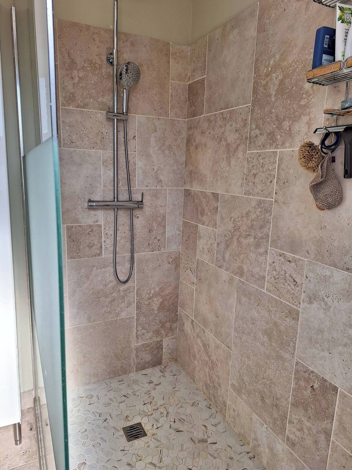A shower with a handheld showerhead and a wall-mounted faucet.