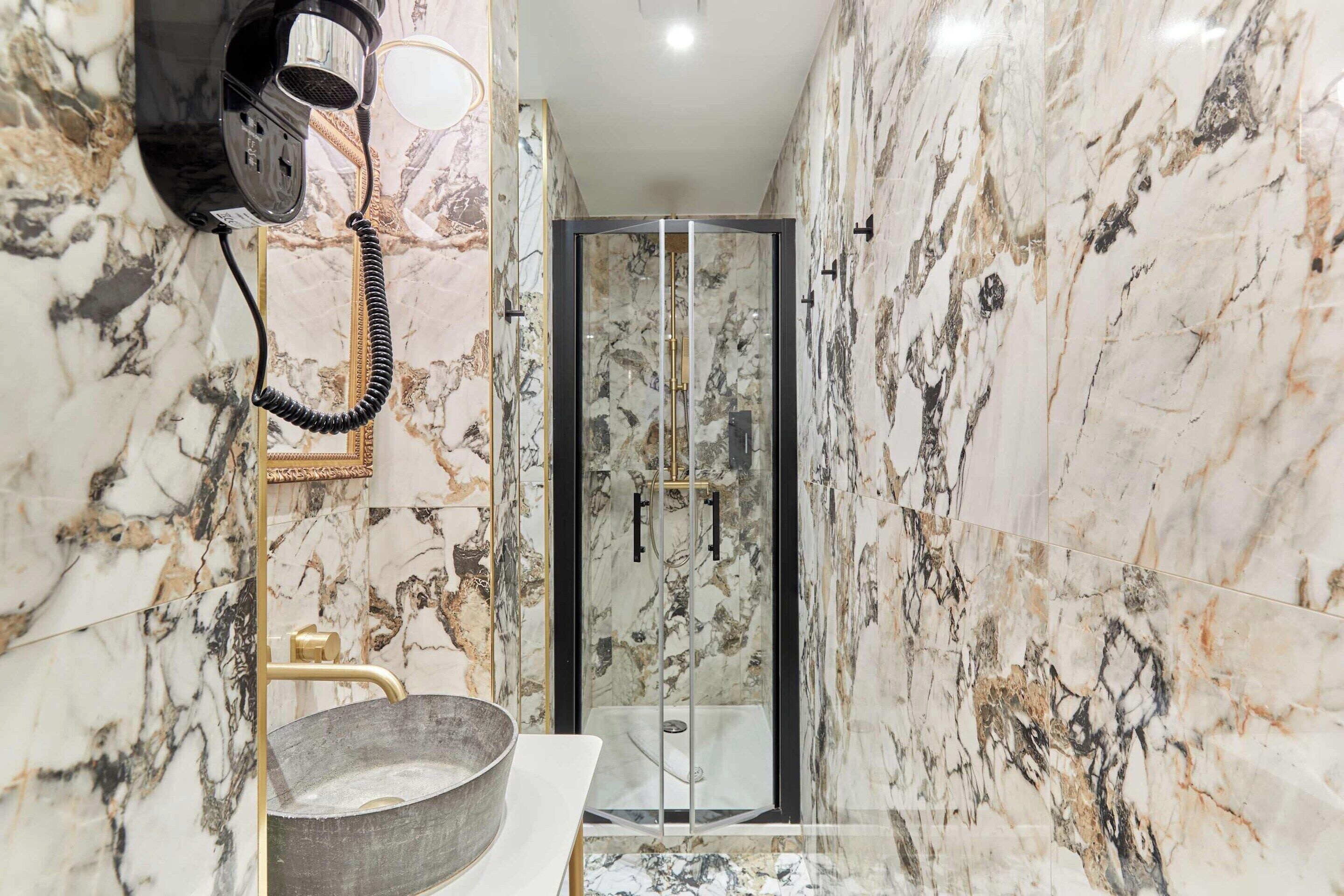 A bathroom with a marble wall, a sink with a gold faucet, and a glass-enclosed shower.