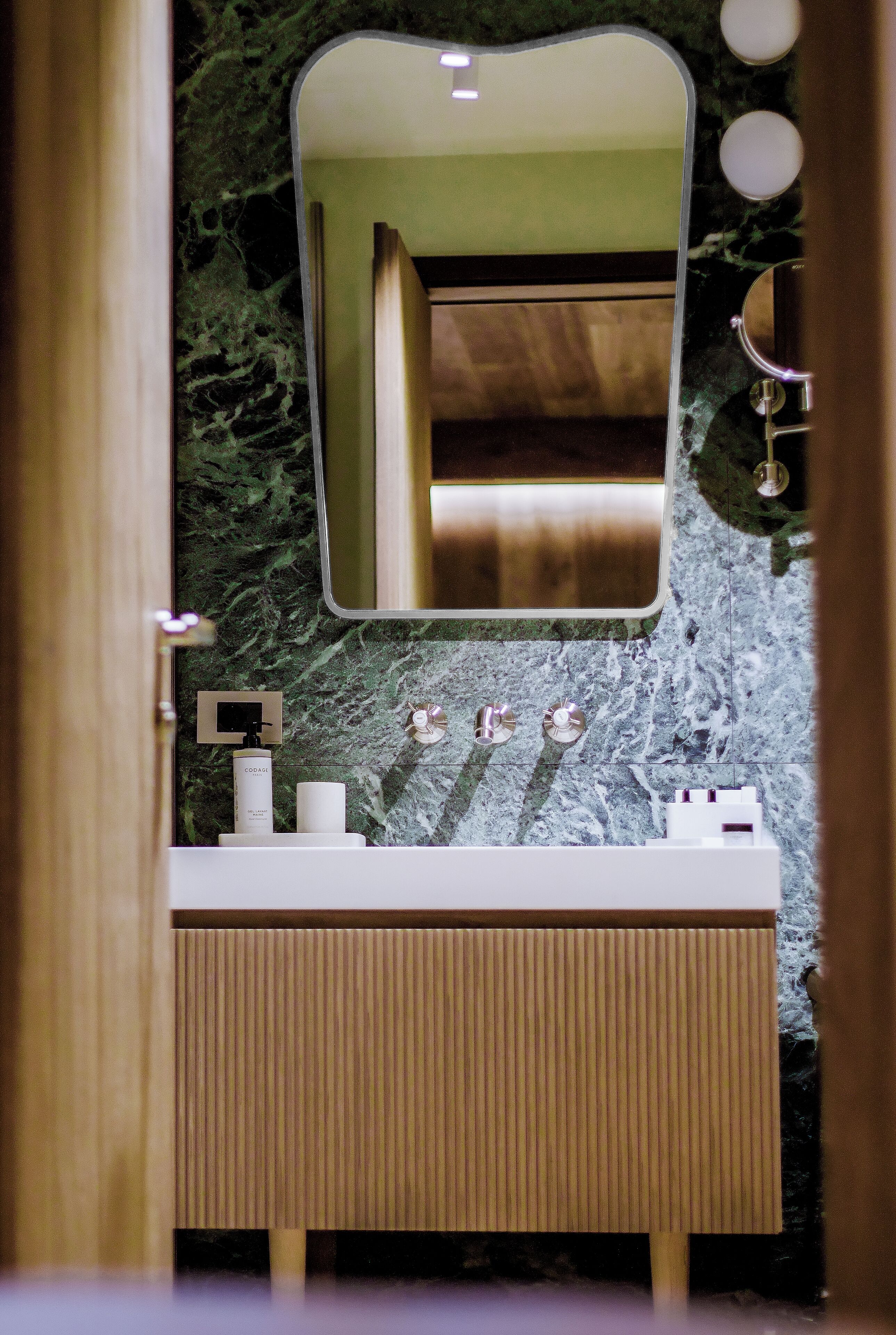 Ein Badezimmer mit Marmorwand, Waschtisch aus Holz, Spiegel und Waschbecken.