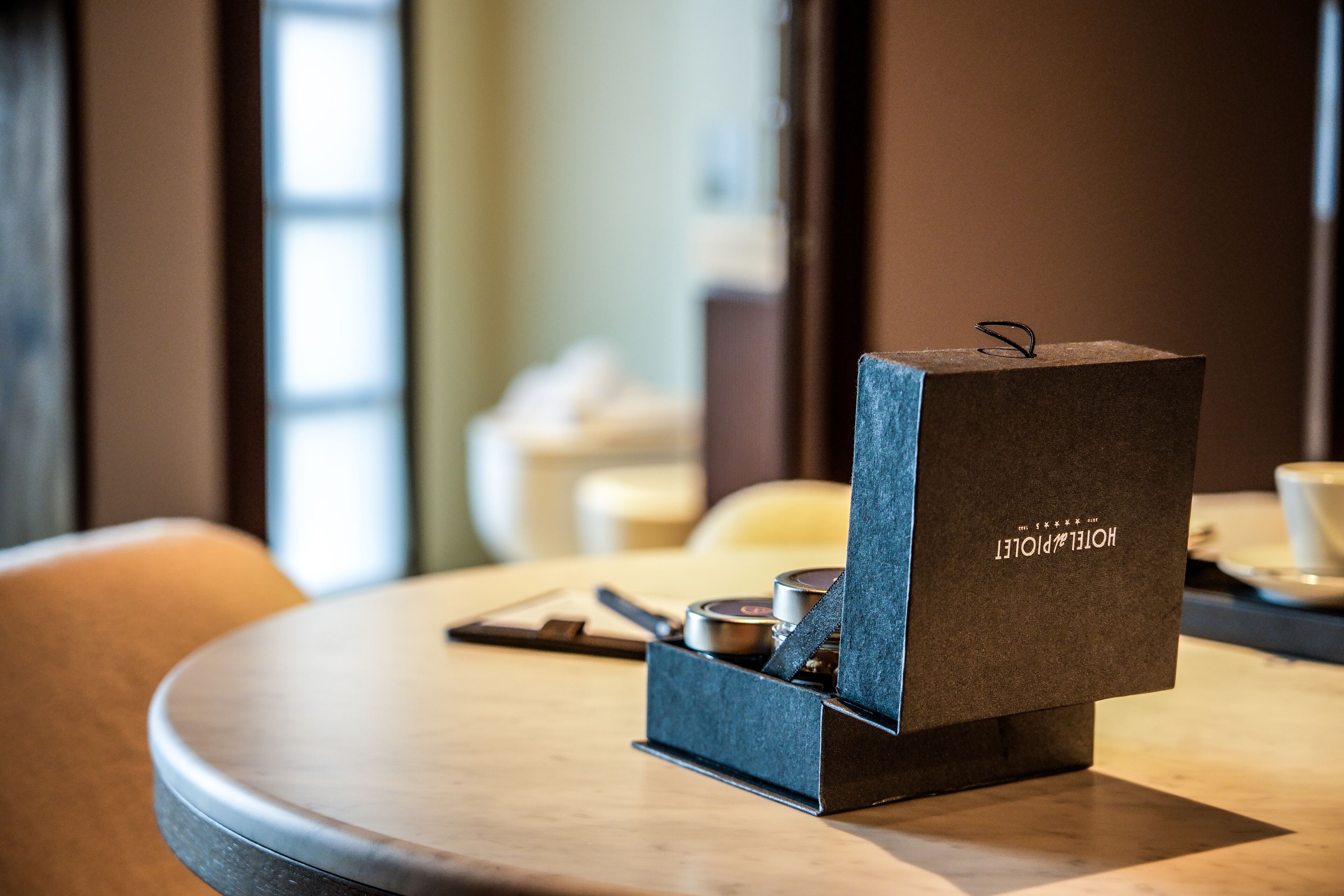 Une boîte cadeau de couleur brun foncé, portant l’inscription « HOTEL POINTER », est posée sur une table ronde, à côté d’un stylo et d’un petit récipient.