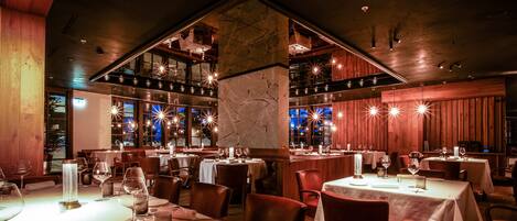 Een restaurant met meerdere eettafels, kaarsen en een hoog plafond met zichtbare balken.