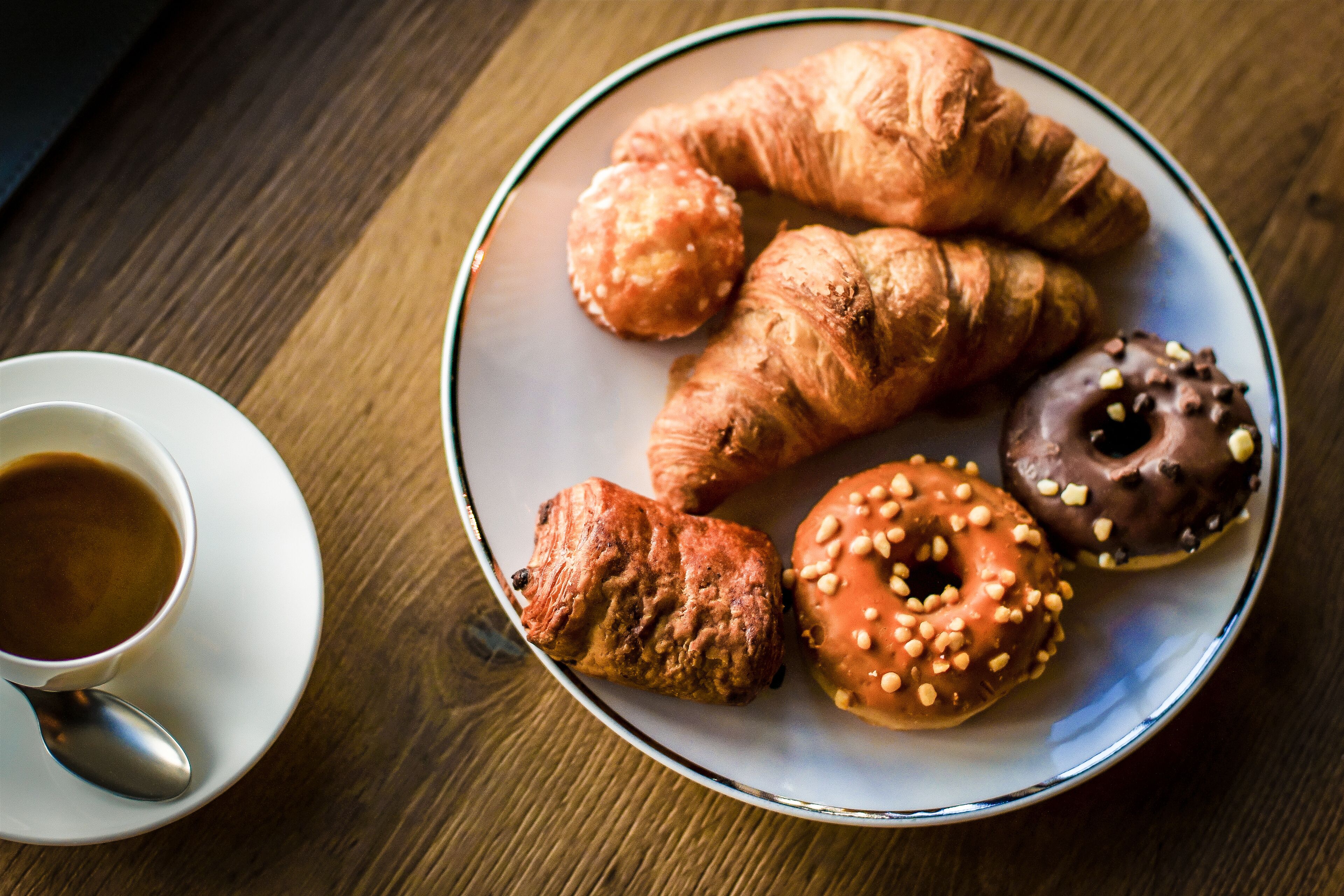 Um prato com croissants e um donut sobre uma mesa de madeira.