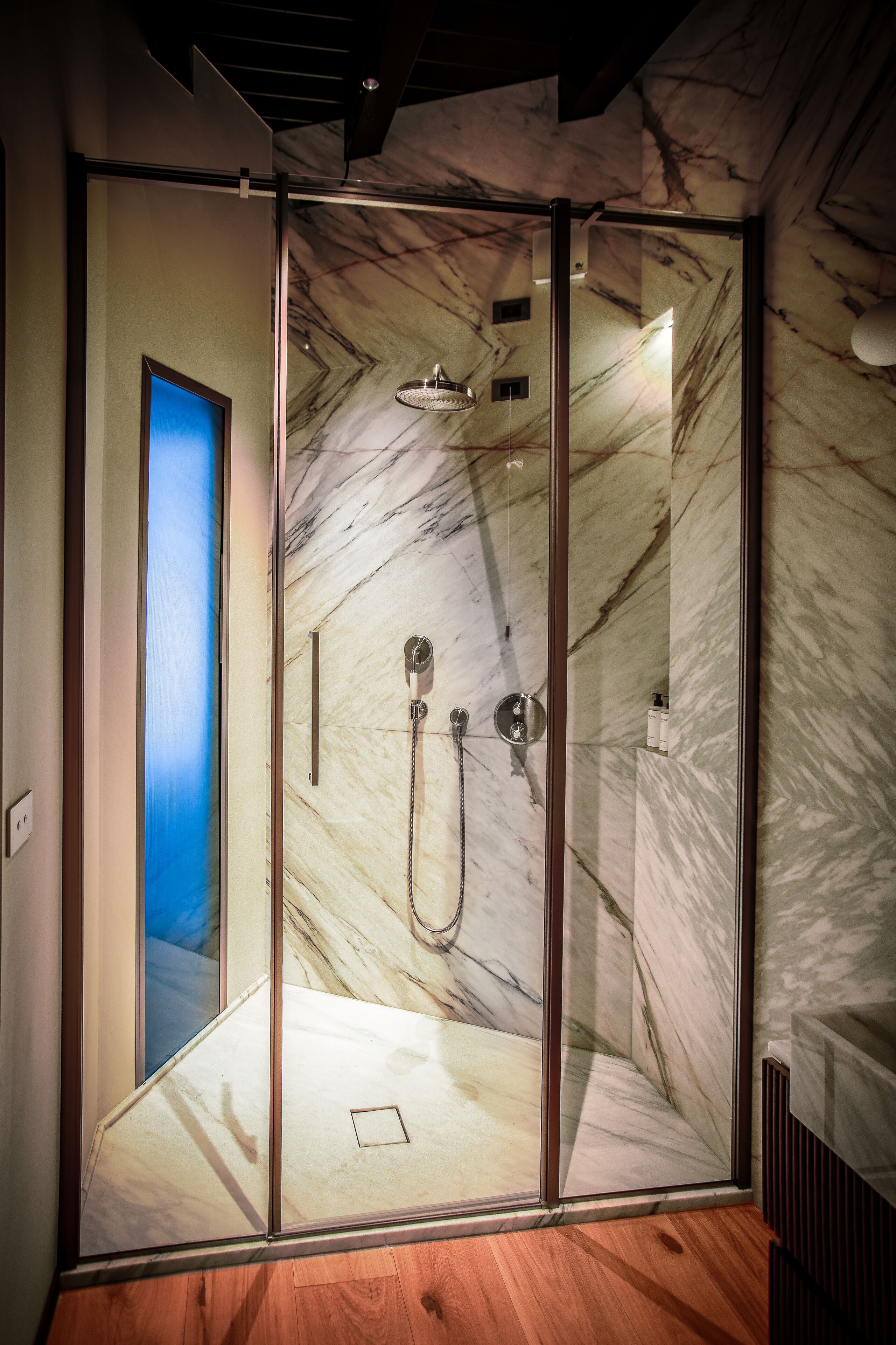 Ein modernes Badezimmer mit einer gläsernen Duschkabine, Marmorwänden und Holzboden.
