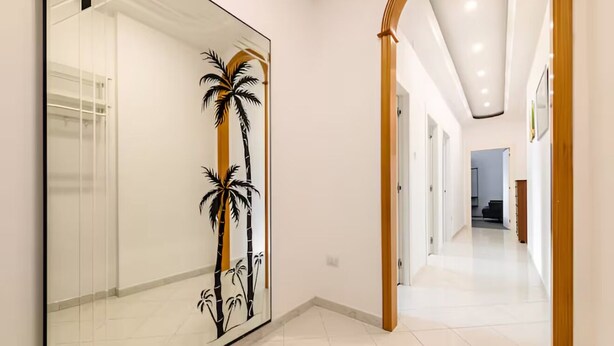 Corredor com porta de vidro com desenho de palmeira, paredes brancas e chão ladrilhado.