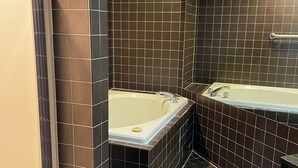 A bathroom with dark brown tiled walls, a white bathtub, and a white sink. - Neat and Clean Rooms that are Affordable! (Hagerstown)