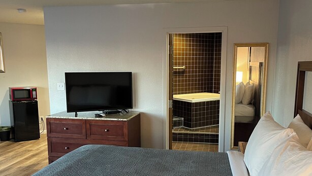 A hotel room with a large bed, a dresser, a television, and a bathroom visible through an open door. - Neat and Clean Rooms that are Affordable! (Hagerstown)