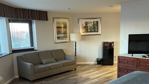 A hotel room with a bed, a sofa, a TV, a microwave, and framed pictures on the wall. - Neat and Clean Rooms that are Affordable! (Hagerstown)