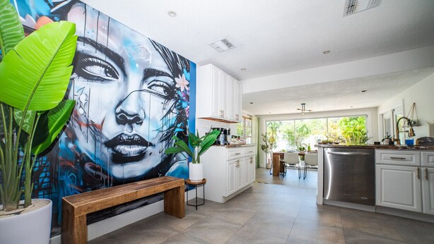 A modern kitchen with white cabinets, a stainless steel dishwasher, and a large mural on the wall. - Chic MangoTree villa/Heated Pool (Fort Lauderdale)