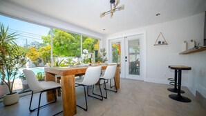 A dining area with a wooden table and chairs, a small bar stool, and a view of a swimming pool and greenery outside. - Chic MangoTree villa/Heated Pool (Fort Lauderdale)