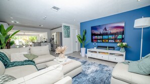 A modern living room with a large flat-screen TV, a white sofa, and a blue accent wall. - Chic MangoTree villa/Heated Pool (Fort Lauderdale)