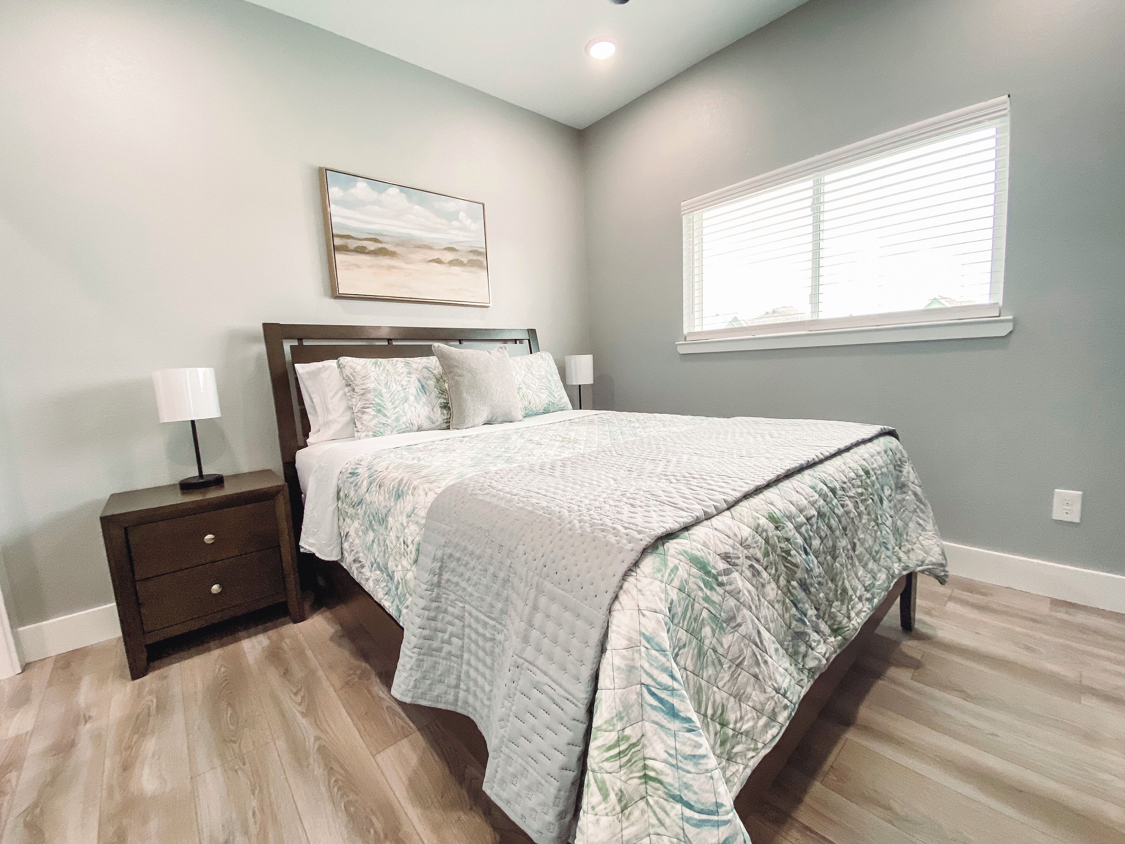 A bedroom with a bed, nightstands, a painting, and a window.