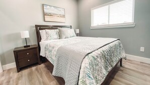 A bedroom with a bed, nightstands, a painting, and a window. - Charming 3-bedroom, pet friendly, house in Crystal Beach. (Bolivar Peninsula)