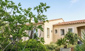 A building with a tiled roof, a window with a potted plant, and a tree with green leaves.