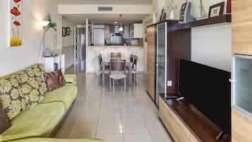 A living room with a sofa, a TV, and a dining area with chairs and a table.