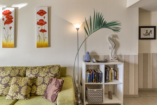 Una sala de estar con un sofá verde, una estantería blanca y dos cuadros florales rojos en la pared.