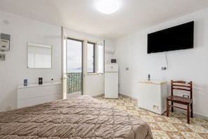 Een slaapkamer met een bed, een televisie, een stoel, een dressoir, een spiegel en een raam.