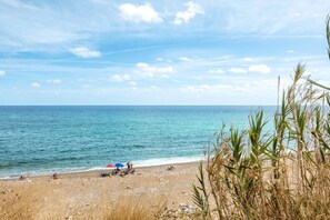 Een strand met heldere lucht, een rustige zee en schaarse begroeiing.