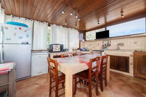 Een keuken met houten kastjes, een betegelde spatwand, een eettafel met stoelen en een koelkast.