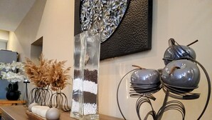 A wooden dresser with decorative items including a clear vase, a metal sculpture, and a tray with white spherical objects. - L'Isle Contemporaine - Spacious 74 M2 Clim Parking Downtown 2 bedrooms (L'Isle-sur-la-Sorgue)