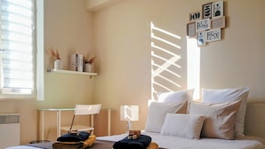 A neatly arranged bedroom with a bed, pillows, a bedside table, a chair, and a shelf with books and decorative items. - L'Isle Contemporaine - Spacious 74 M2 Clim Parking Downtown 2 bedrooms (L'Isle-sur-la-Sorgue)