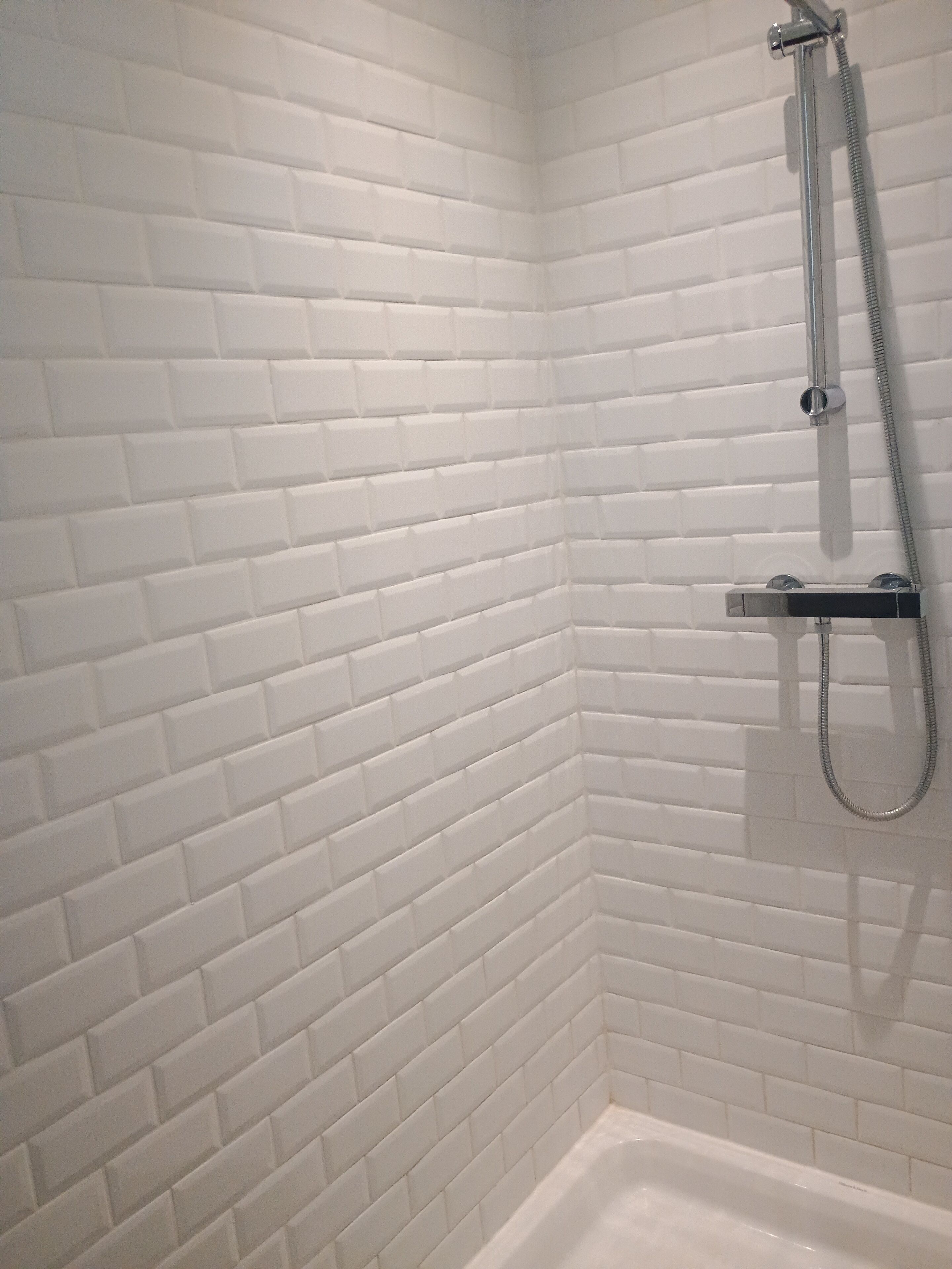 A corner of a bathroom with white tiled walls and a shower area.