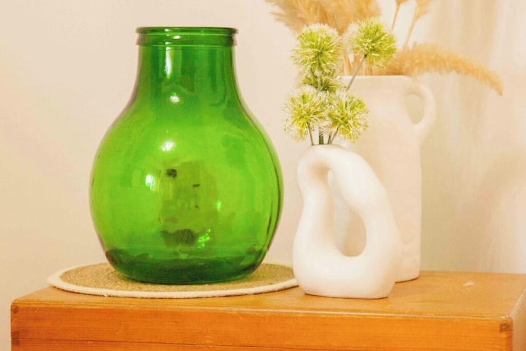 Un vaso di vetro verde e una brocca di ceramica bianca con fiori su un tavolo di legno.