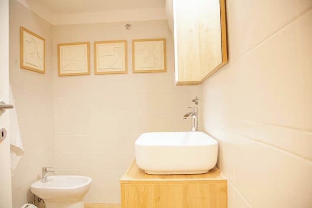 Un baño con un lavabo blanco, una pileta pequeña y tres cuadros en la pared.