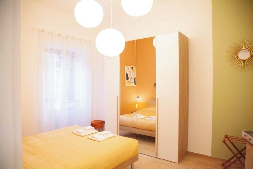 Quarto com cama, guarda-roupa, espelho e luminária suspensa.
