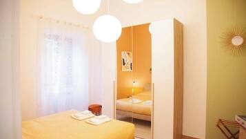 Quarto com cama, guarda-roupa, espelho e luminária suspensa.