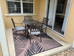 A patio with a round table and four chairs, a patterned rug, and a window with blinds. - Luxury Townhome on reunion resort (Kissimmee)