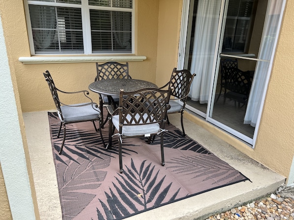 Un patio con una mesa redonda y cuatro sillas, un tapete estampado y una ventana con persianas.