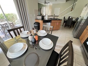 Un comedor con una mesa preparada para cuatro, una cocina al fondo y una escalera que lleva a otro nivel.