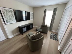 A living room with a flat-screen TV, a black entertainment unit, two armchairs, a glass coffee table, and a patterned rug. - Luxury Townhome on reunion resort (Kissimmee)