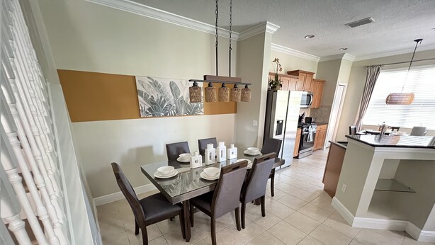 A dining area with a table set for four, a kitchen in the background, and a view of the outside through a window. - Luxury Townhome on reunion resort (Kissimmee)