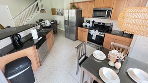 A modern kitchen with a dining area, featuring stainless steel appliances, wooden cabinets, and a black countertop. - Luxury Townhome on reunion resort (Kissimmee)