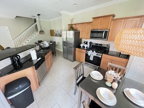 A modern kitchen with a dining area, featuring stainless steel appliances, wooden cabinets, and a black countertop. - Luxury Townhome on reunion resort (Kissimmee)