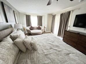 Een ruime hotelkamer met een groot bed, een ronde zithoek, een televisie en een plafondventilator.