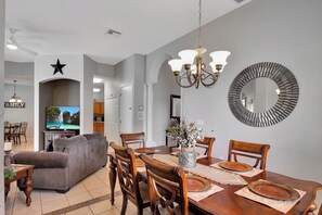 Ein Essbereich mit Holztisch, Stühlen und einer Chandelier. Im Hintergrund befindet sich ein Fernseher und eine Stern-Dekoration an der Wand.
