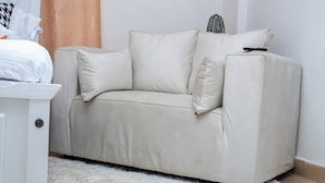 A beige sofa with a remote control on it, positioned against a white wall. - Couple Friendly Studio Apartment In Pangani (Nairobi)
