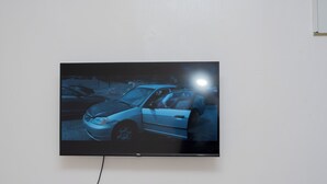 A flat-screen TV mounted on a wall displaying a nighttime scene with a car. - Couple Friendly Studio Apartment In Pangani (Nairobi)